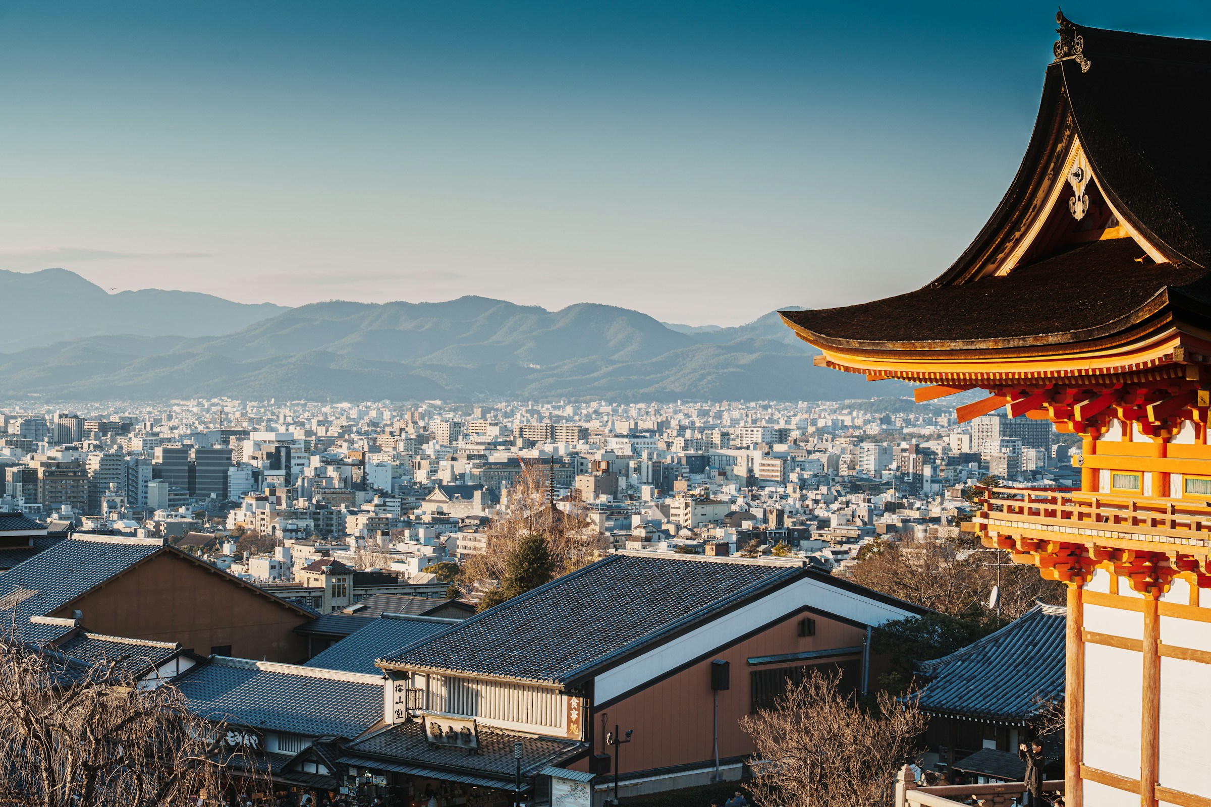 Kyoto cityscape, temple rooftops, and mountains beneath a dramatic sky